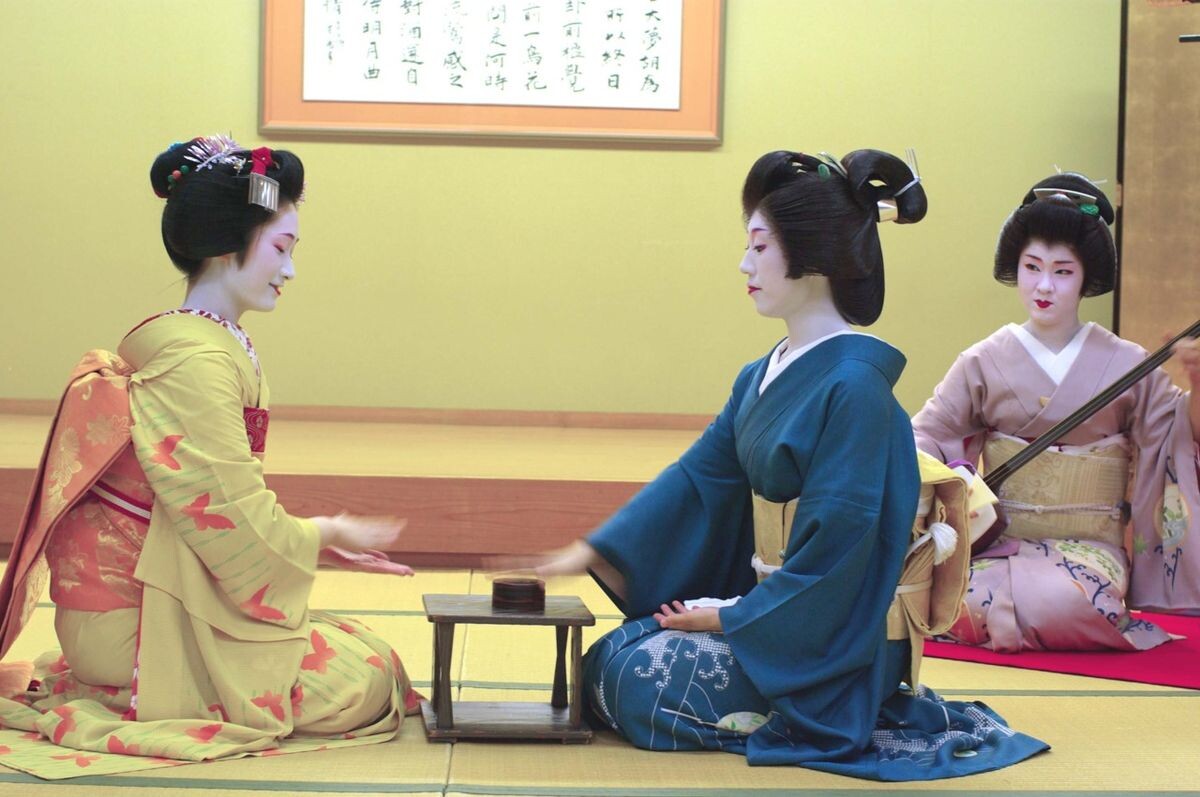 Майко и гейша играют в традиционную игру Компира фунэ-фунэ, сзади – гейша с сямисэном