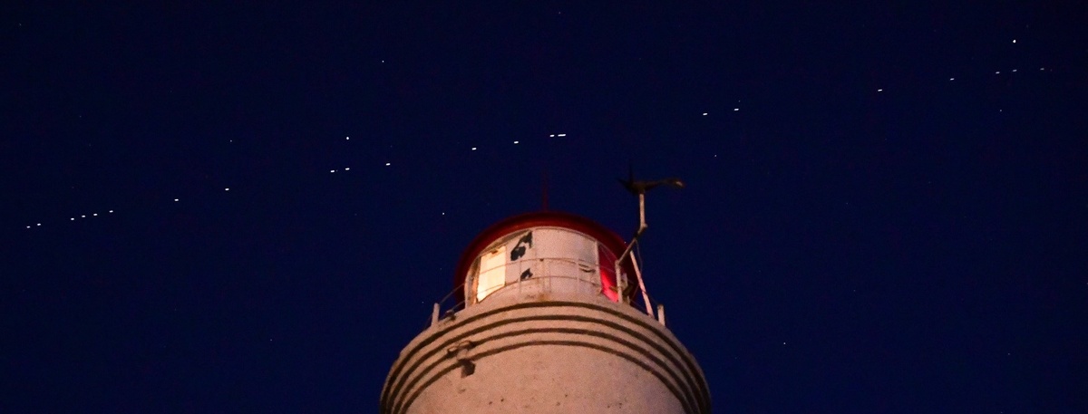   Спутники связи Starlink (белые точки в небе над маяком) проходят по орбите Земли, архивное фото. Автор фото: Юрий Смитюк / ТАСС