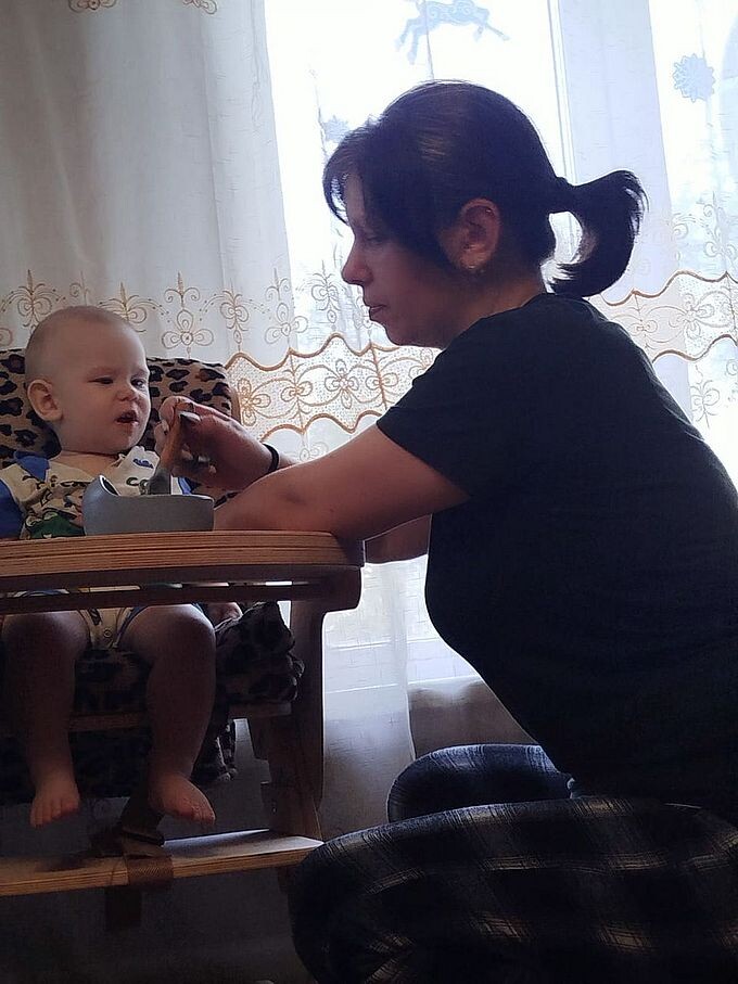 Мама кормит сына, сидящего в стульчике для кормления