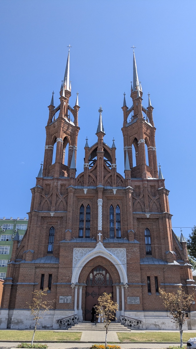 Вид на польский костёл с улицы Фрунзе. Высокие шпили и красный кирпич выделяются среди обычных городских домов. Контраст, который сразу приковывает взгляд.