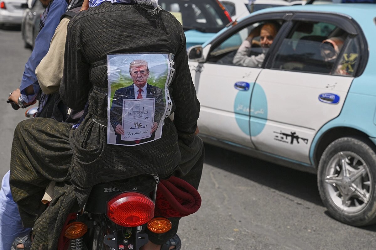   Мужчина в куртке с изображением президента США Дональда Трампа, держащего бумагу с датой возвращения «Талибана» ко власти со словами «День нашего побега». Кабул, Афганистан, 15 августа 2025 года 
Nava Jamshidi / AP