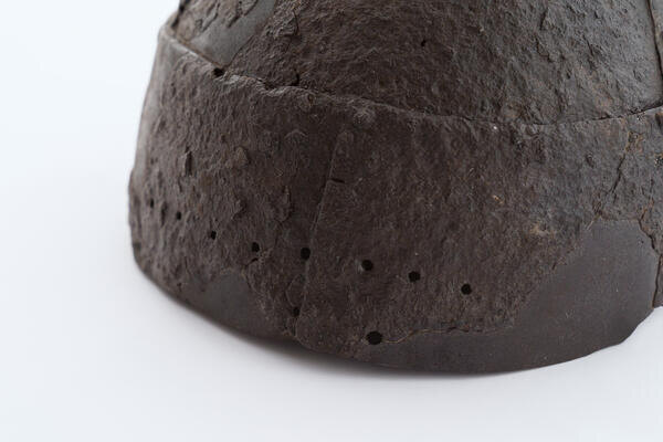 Шлем низкий, с налобной пластиной ободом, склепан из нескольких пластин. Основание овальное с мелкими круглыми сквозными отверстиями по краю для крепления.