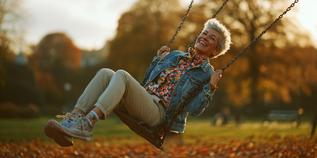 "Женщина среднего возраста с короткими седыми волосами качается на качелях в осеннем парке и улыбается — символ лёгкости и радости жизни на кето диете для женщин, несмотря на её особенности и противопоказания."