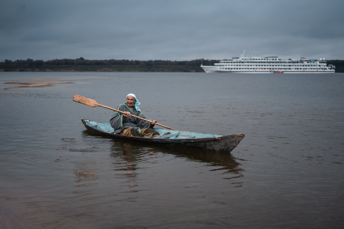 Представитель кетов на традиционной лодке на фоне круизного теплохода. Фото автора