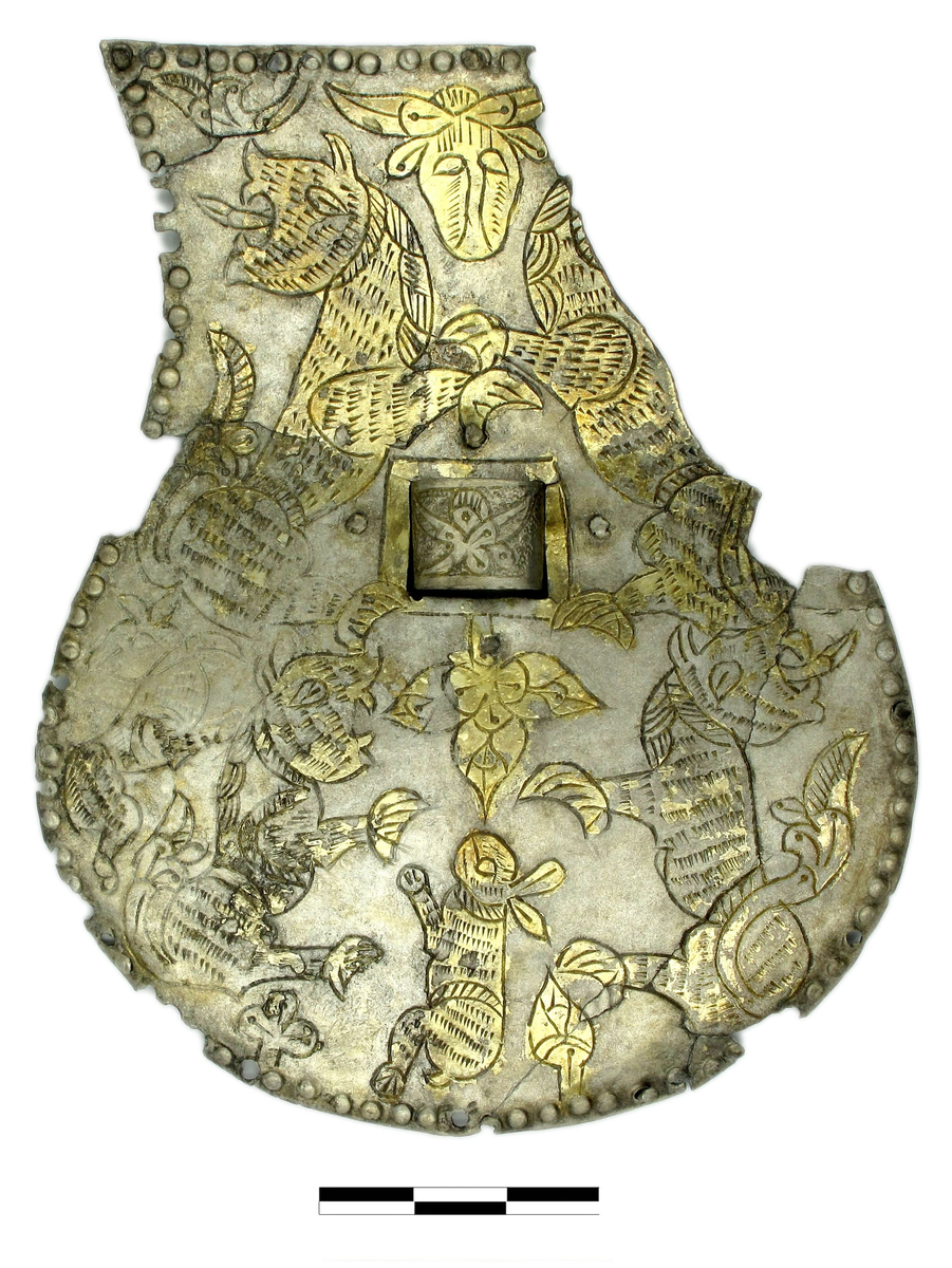 Накладка - деталь украшения сумки, Северный Кавказ(?), IX-X вв, белый металл, литье, золочение, травление, 11,4х9,1, 3,1х1,2 см, Подполуовальной формы, с квадратным отверстием в центре, с множеством фрагментов клепок по краю, с зооморфным орнаментом в виде зайца, коровы и хищных млекопитающих и растительным орнаментом в виде листьев и трилистников