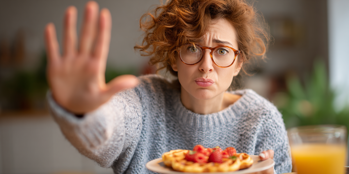 "Женщина в очках с грустным выражением лица отказывается от вафель с ягодами и апельсиновым соком — запрещённые продукты на кето диете."