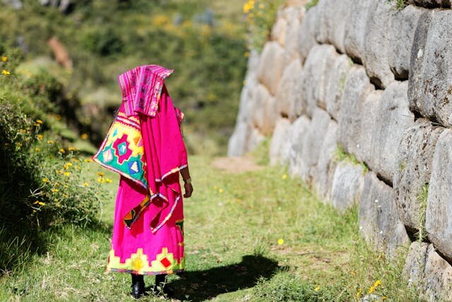 Женщина в яркой национальной одежде идёт по древней каменной улице в Перу