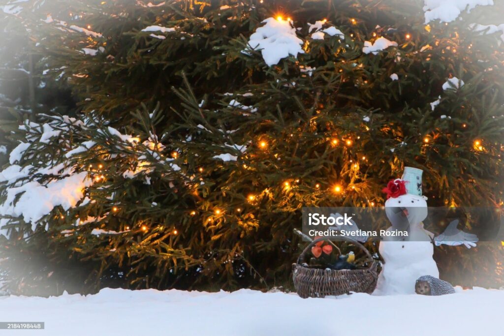    Winter decor. Snowman against the background of a Christmas tree. Funny snowman. Christmas mood. The snowman is in focus; in the background, an electric garland is lit in warm yellow color. Редакция газеты