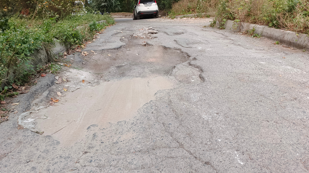 Яма с торца дома тоже разрослась, сюда жильцы периодически сваливают строительный мусор от ремонта жилых помещений.  В данный момент видно, что часть ямы подсыпали песком. Это хоть как-то спасает личный транспорт жителей от ободранного днища авто, погнутого порога  или от оторванного глушителя.