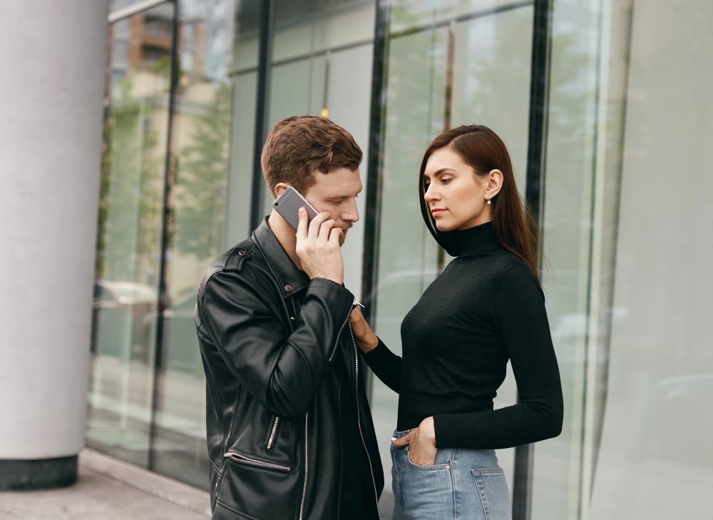 Молодая женщина разговаривает с мужчиной, который держит телефон — недопонимание и напряжённый момент в отношениях