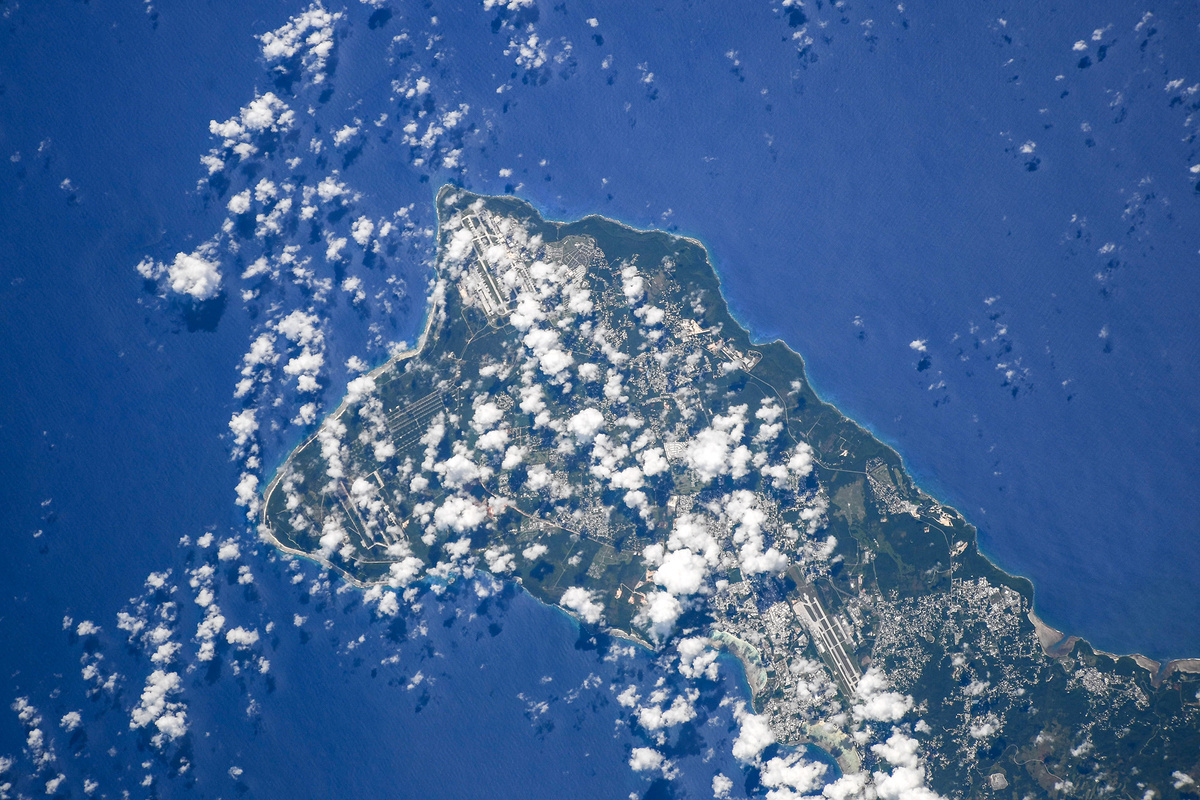 Частично над островом лежат белые пушистые облака, причём их тень не слишком сгущена, так что детали рельефа просматриваются.