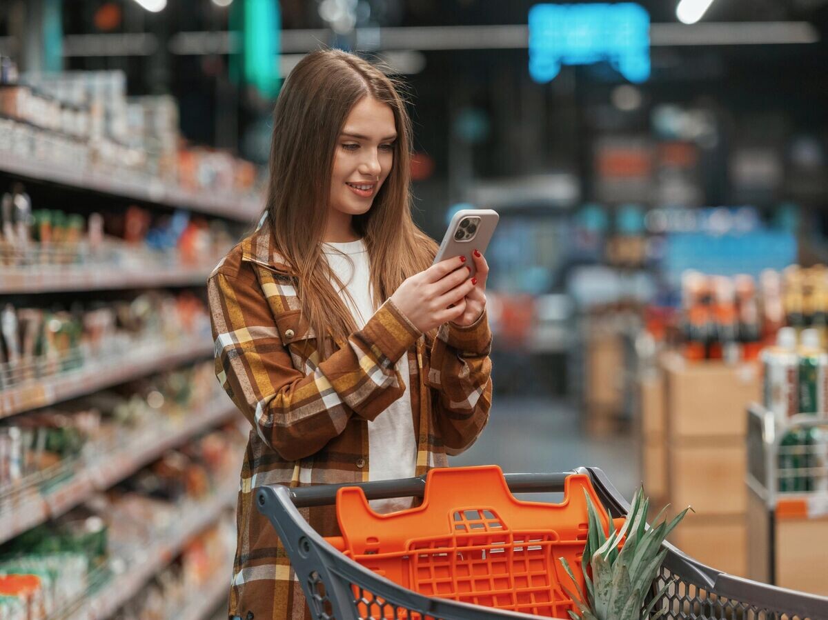    Девушка использует смартфон в супермаркете© iStock.com / standret