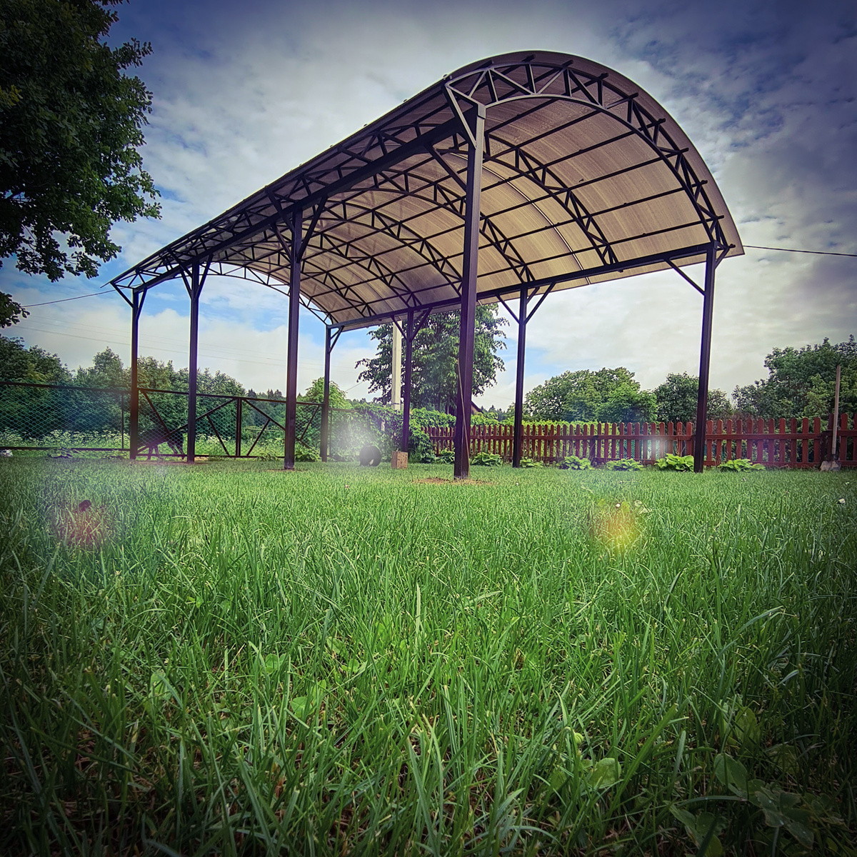 Навес для автомобиля из металла и поликарбоната, установленный во дворе частного дома. Прочная конструкция с камерной покраской (эпоксидный грунт, полиуретановая эмаль с отвердителем) защищает машину от солнца и осадков. Проект и монтаж — компания ARTZHELEZO.