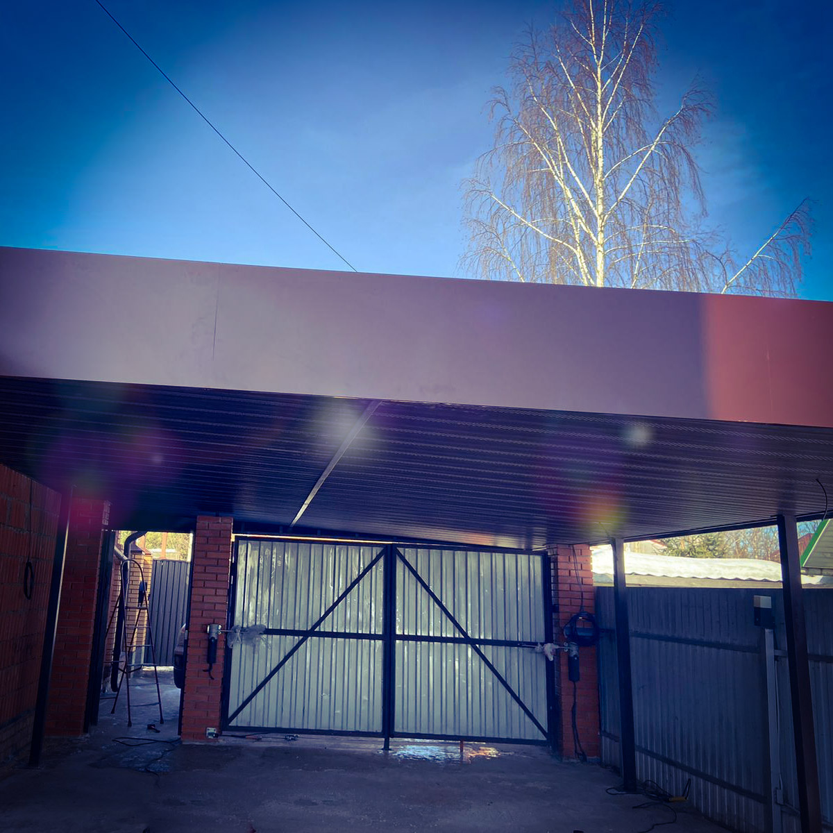 Навес для автомобиля из металла и поликарбоната, установленный во дворе частного дома. Прочная конструкция с камерной покраской (эпоксидный грунт, полиуретановая эмаль с отвердителем) защищает машину от солнца и осадков. Проект и монтаж — компания ARTZHELEZO.