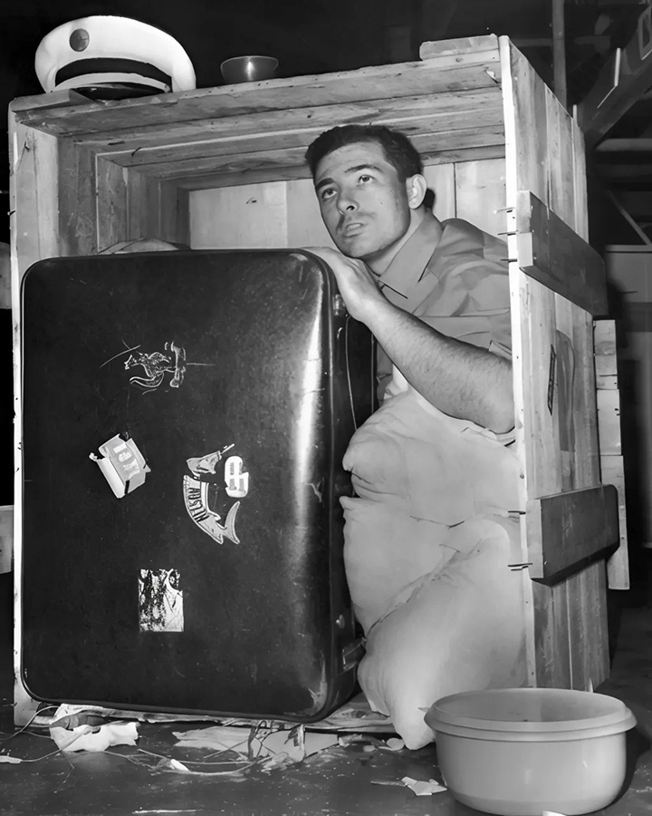 Грузчик Гэри Хэтч (на фото) демонстрирует, как он обнаружил безбилетного пассажира Брайана Робсона, сидящего внутри этого грузового ящика в аэропорту Лос-Анджелеса