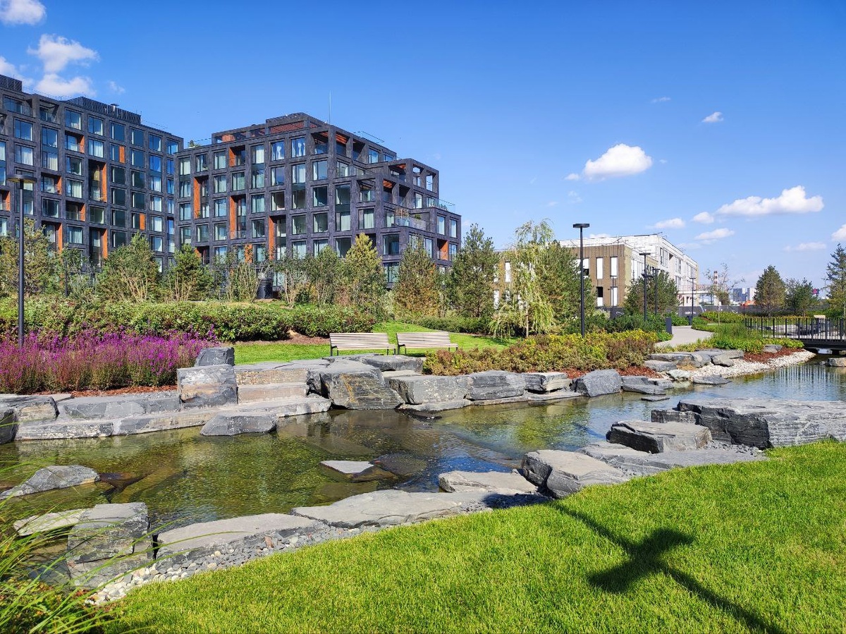 Первым делом бросилось в глаза продуманное ландшафтное оформление: зеленые газоны, аккуратно высаженные кустарники, тенистые аллеи. Будто случайно забрела в парк, а не оказалась посреди бетонных джунглей столицы. Очень приятно пройтись среди зелени, отдыхая душой и телом после рабочей рутины.

Помимо природной гармонии глаз радует современная архитектура комплекса. Фасады зданий выглядят стильно и современно, без кричащих деталей и безвкусицы. Внутри дома также всё выполнено со вкусом: просторные холлы, чистота и ухоженность подъездов вызывают приятное удивление.

Особенно порадовала забота о комфорте будущих жителей. Прямо на территории комплекса обустроены игровые площадки для малышей, беговые и велосипедные маршруты, уличные тренажёры. Можно привести ребёнка погулять, заняться йогой на свежем воздухе или совершить утреннюю пробежку без выхода за пределы квартала.
