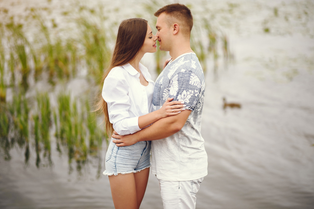Молодая пара обнимается и смотрит друг другу в глаза на берегу водоёма, символизируя романтическую влюблённость и близость