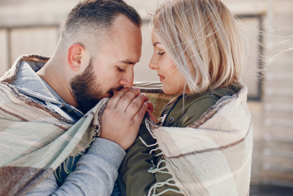 Мужчина и женщина укутались в плед и смотрят друг на друга с теплотой — символ того, что любовь растёт и развивается вместе с нами.