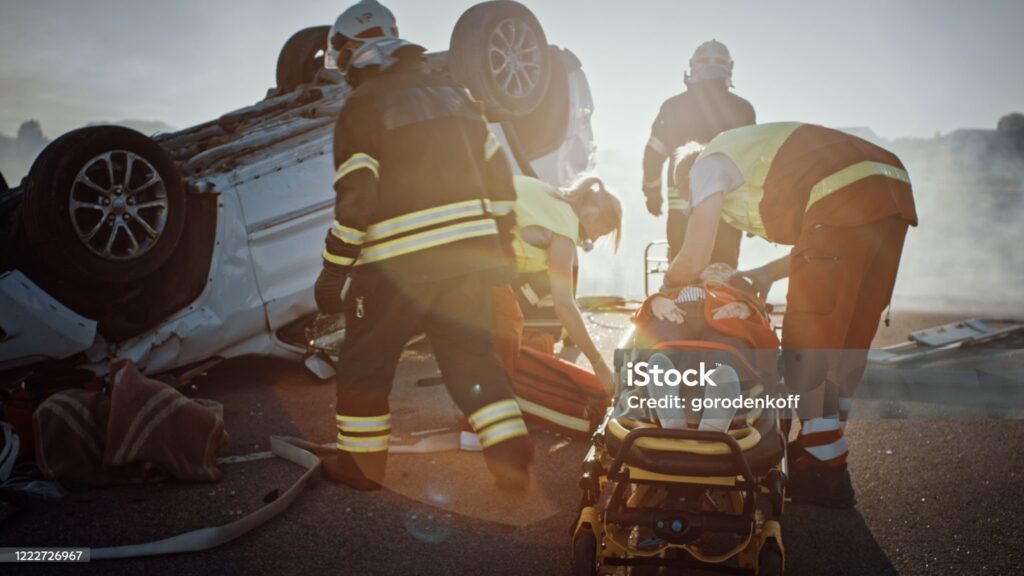    On the Car Crash Traffic Accident Scene: Rescue Team of Firefighters Pull Female Victim out of Rollover Vehicle, They Use Stretchers Carefully, Hand Her Over to Paramedics who Perform First Aid Редакция газеты