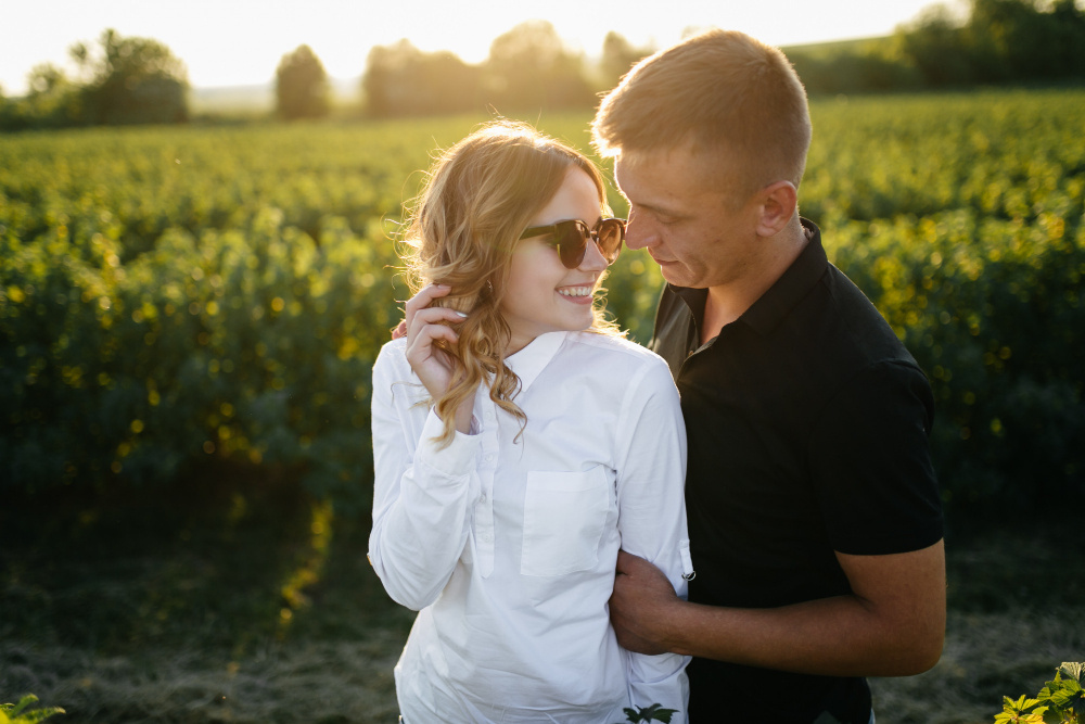 Влюблённая пара обнимается на закате в поле, смотря друг другу в глаза и наслаждаясь моментом близости.