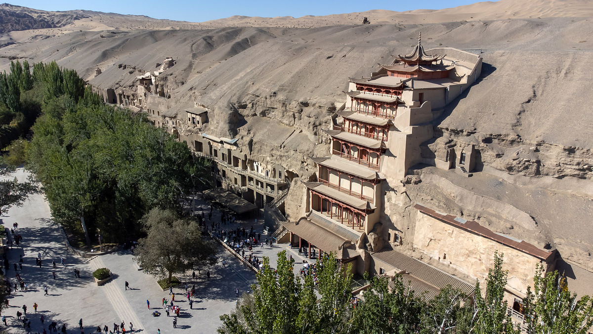 Многоярусный деревянный фасад в форме пагоды, построенный для защиты гигантского Будды, стал культовой особенностью пещер Могао в Дуньхуане, провинция Ганьсу.