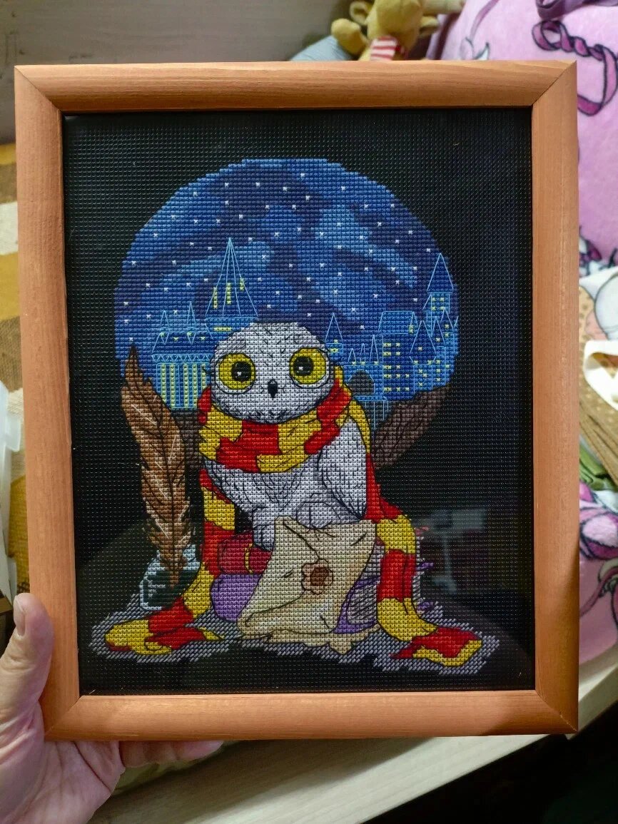 Вышитая сова в шарфе Гриффиндора, держащая письмо, на фоне Хогвартса и звездного неба. Это готовая работа, выполненная по схеме для вышивания Анны Шишкиной