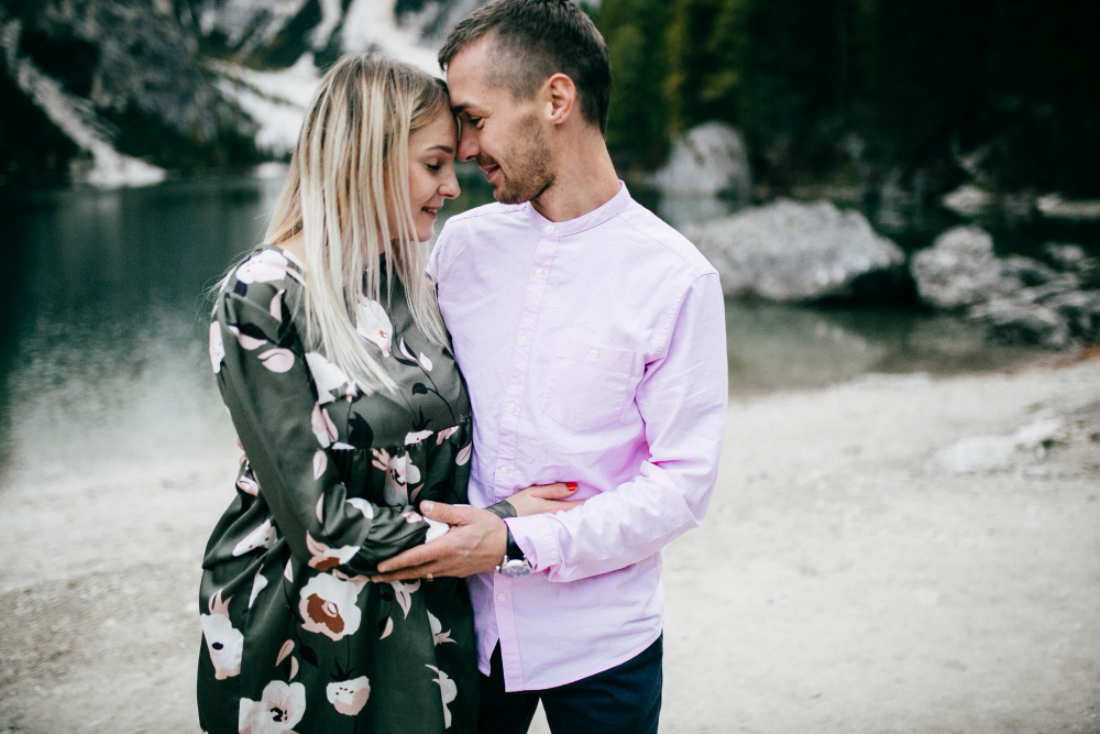 Пара обнимается и улыбается на фоне озера и гор, наслаждаясь моментом близости и тепла.