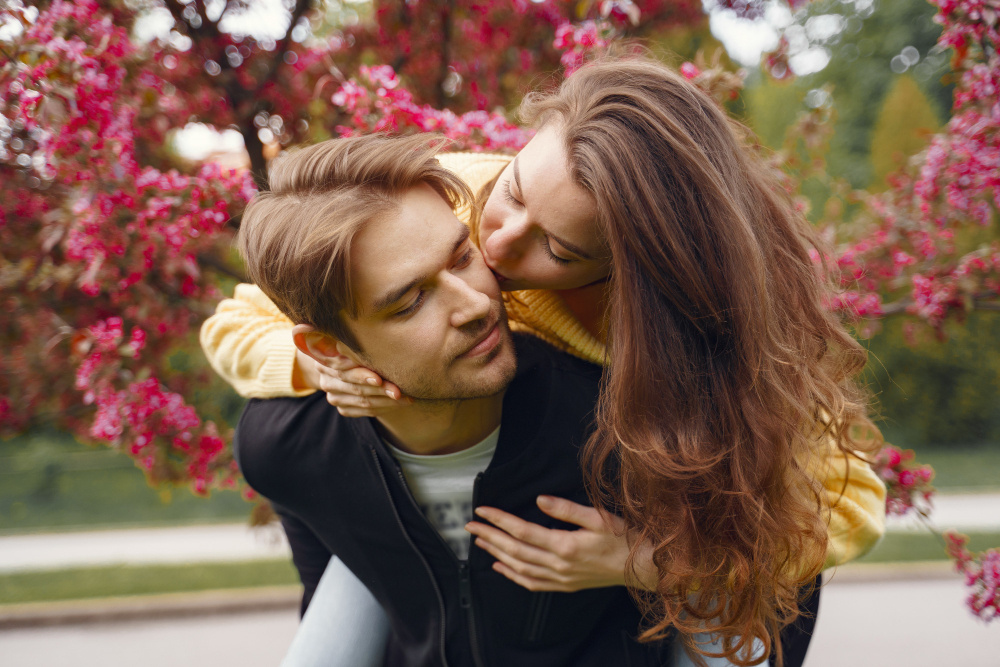 «Девушка обнимает молодого человека на прогулке в парке с цветущими деревьями