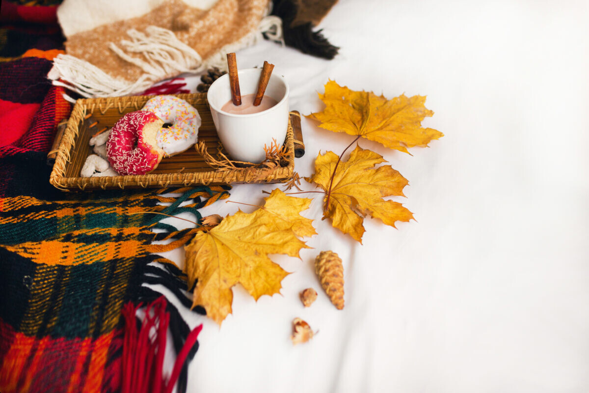    cozy autumn image of tasty breakfast in bed on wooden tray with cup of cacao, cinnamon, cookies and glazed donuts.Warm toned colors, top view, yellow leaves and cones. Ксения Кузнецова