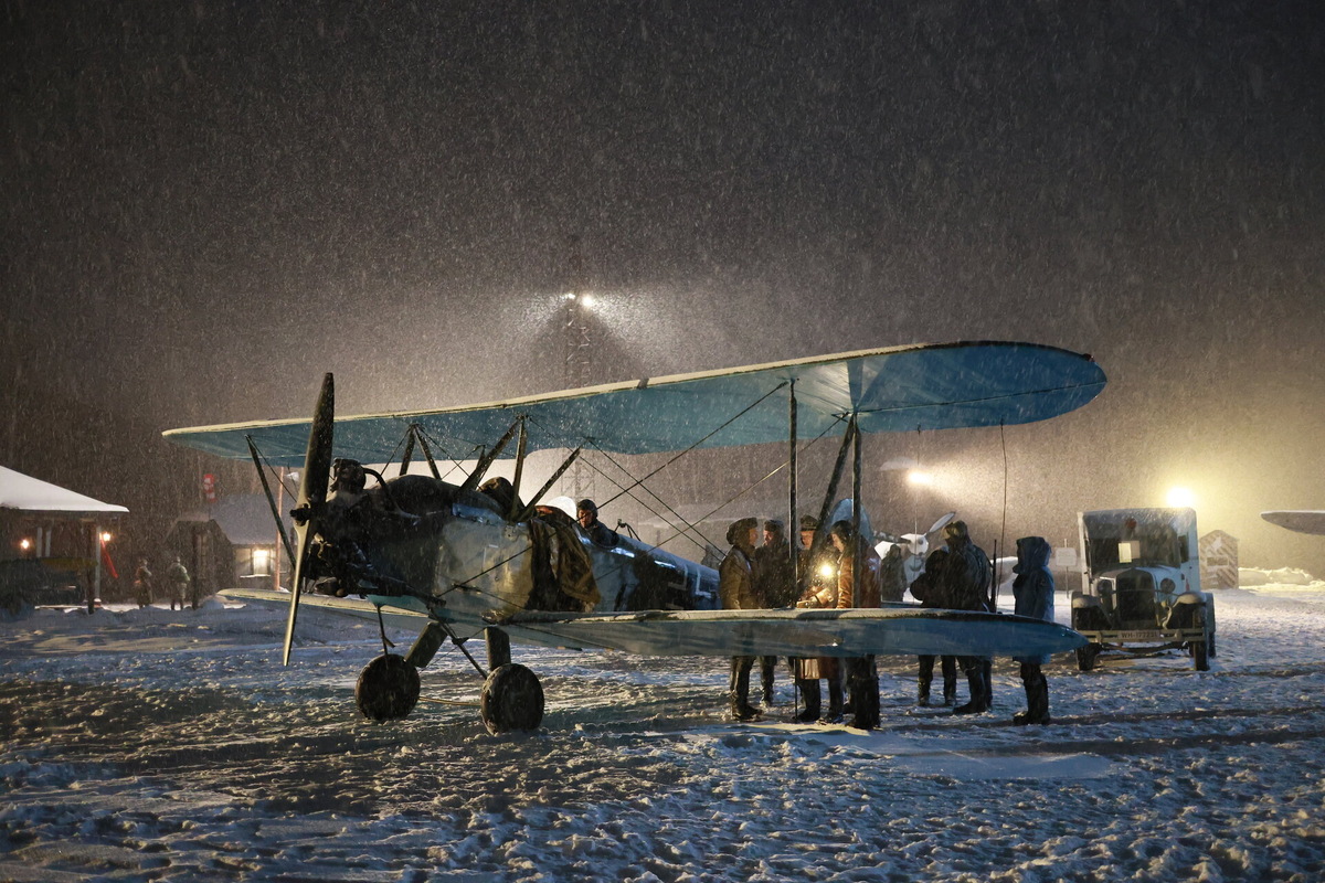 Ночная сцена на аэродроме, старый биплан и лётчики перед вылетом в снегопад.