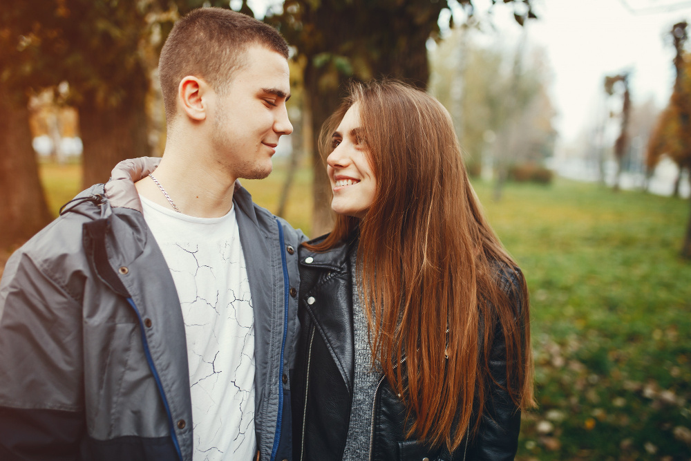 Молодая пара улыбается и смотрит друг на друга в парке, символизируя новые отношения и готовность к любви после развода