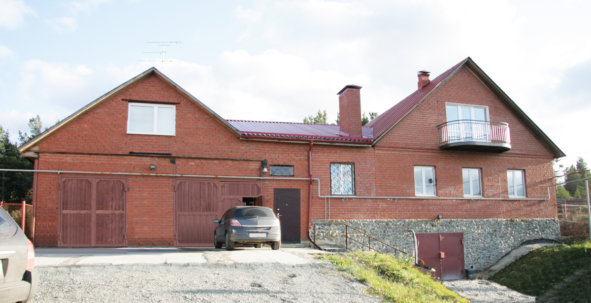 Кирпичный фасад, белые рамы окон, несимметричные красные ворота, чёрная входная дверь без козырька (скат кровли устроен так, что на входящего льёт дождь со всей кровли), невыразительные перильца.