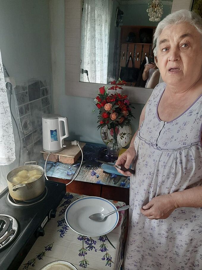 Пожилая женщина варит картофель на плитке