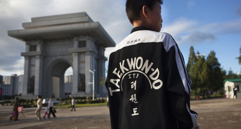 Молодой человек в спортивном костюме тхэквондо ИТФ на фоне триумфальной арки в Пхеньяне