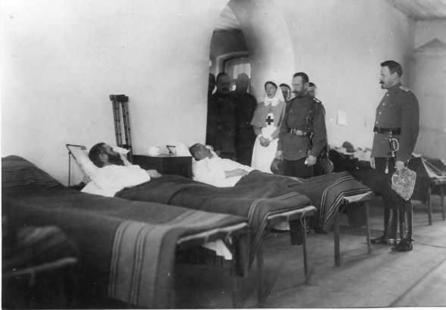 Посещение императором Николаем II города Ровно. Император Николай II с сестрой, вел. княгиней Ольгой Александровной, обходят раненых во время посещения госпиталя Евгеньевской общины Красного Креста имени вел. княгини Ольги Александровны, в котором вел. княгиня с начала войны работает рядовой лазаретной сестрой милосердия. Присутствует дворцовый комендант генерал-майор свиты В.Н.Воейков