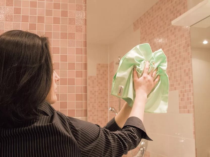 Чистка зеркала в ванной с использованием мягкой тряпки.