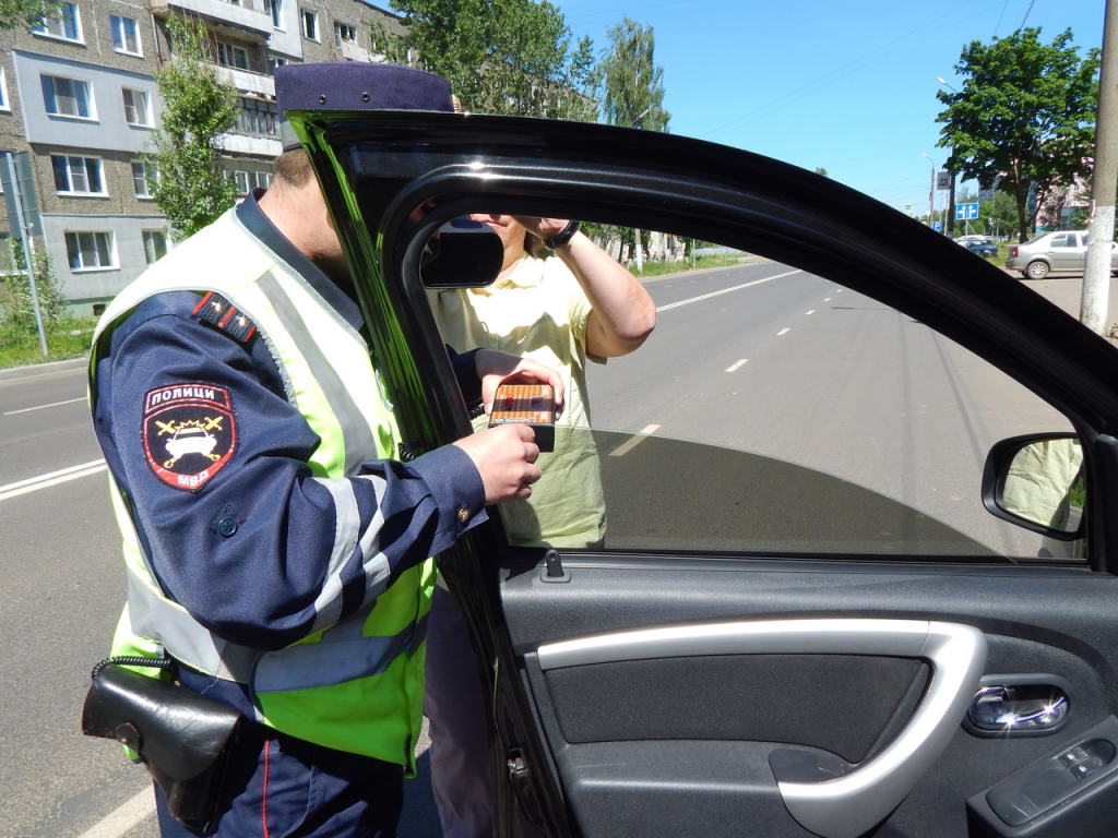 Инспектор ДПС производит замер светопропускаемости переднего бокового стекла водительской двери.