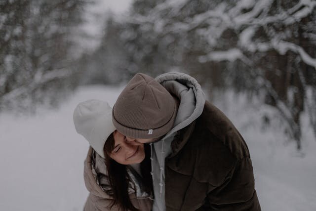 Мужчина обнимает женщину на зимней улице, они улыбаются — тёплые чувства и любовь в холодное время года