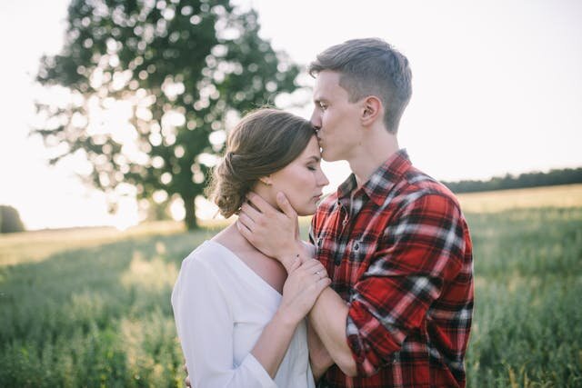 Мужчина нежно целует женщину в лоб на закате — доверие и забота в отношениях