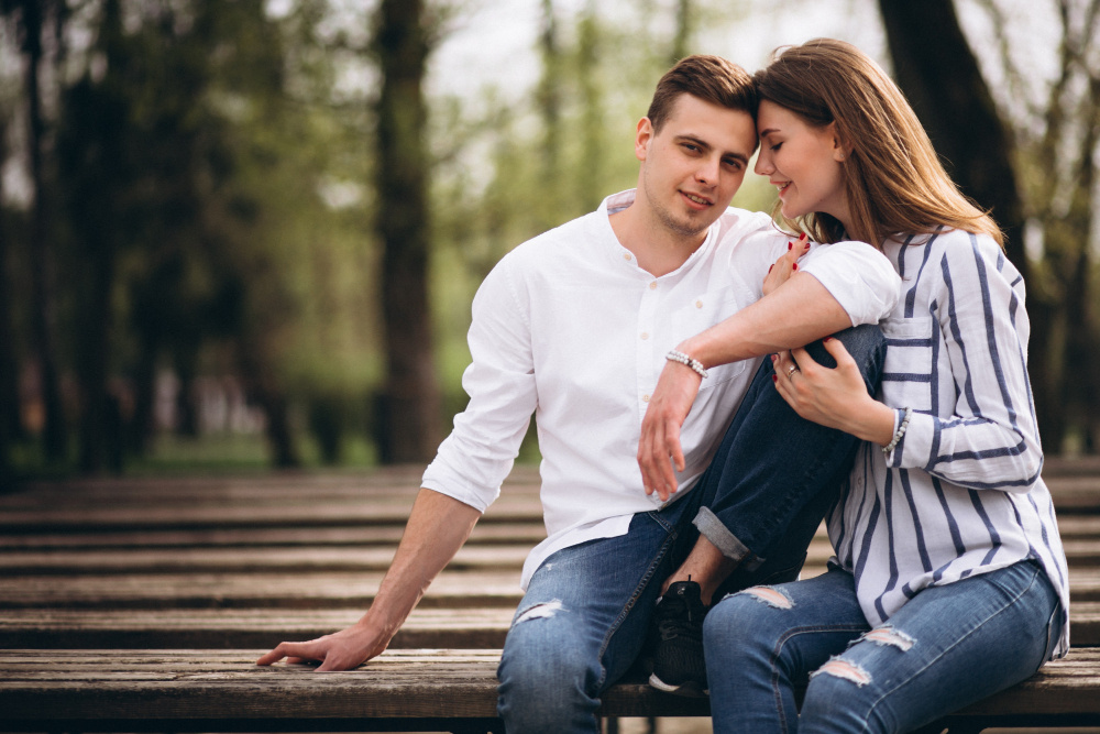 Мужчина и женщина сидят на скамейке в парке, улыбаются и держатся за руки — символ нежности и попытки вернуть тепло в отношениях.