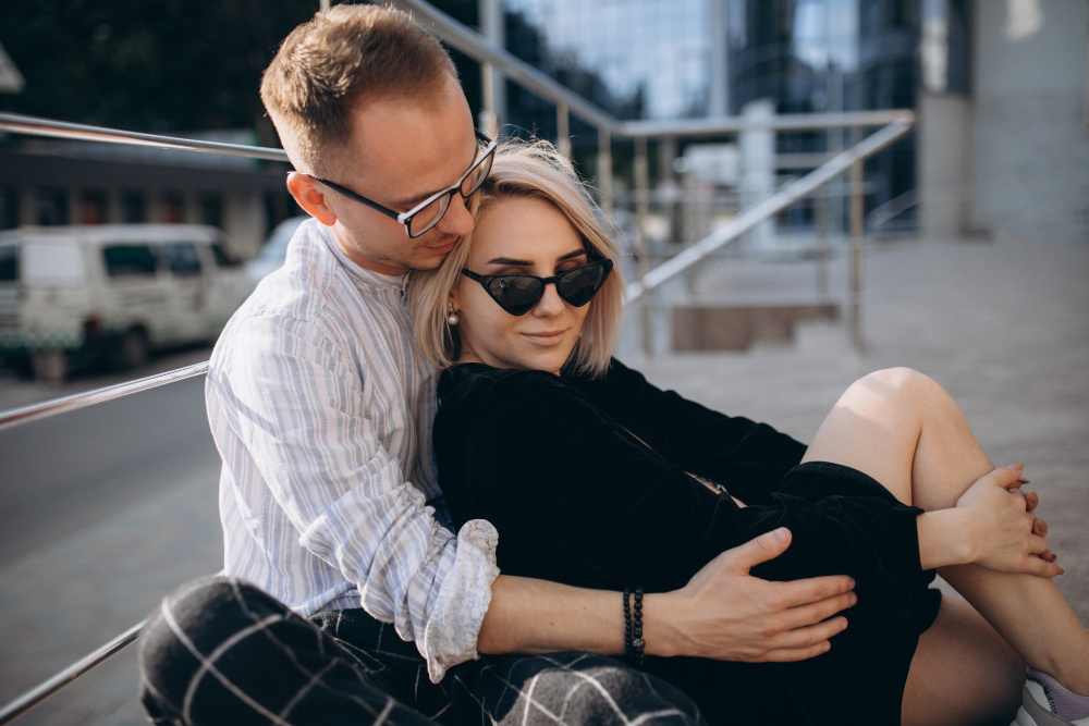 Мужчина обнимает женщину, сидящую у него на коленях на улице, — символ доверия, тепла и стремления преодолеть страх ответственности в любви.