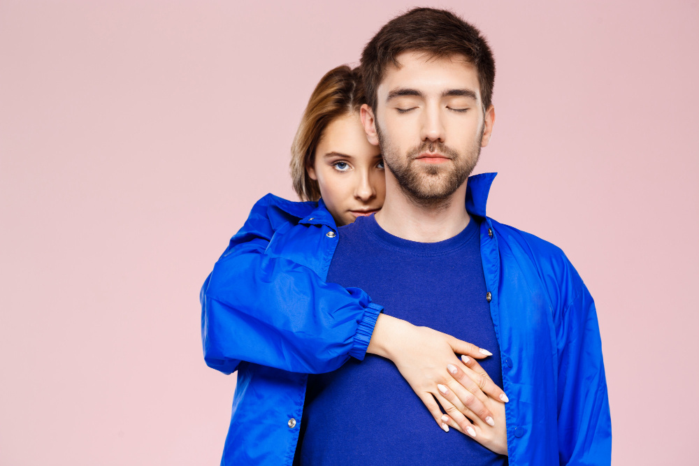 Женщина обнимает мужчину со спины, он стоит с закрытыми глазами — символ доверия, поддержки и преодоления страха в любви.