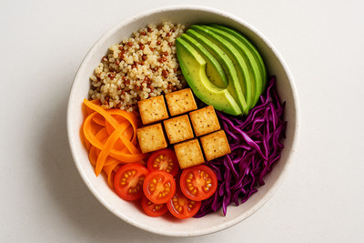 "Top-down photo of a vegan protein bowl with quinoa, avocado, tofu and colorful vegetables, natural light, minimalistic style, 4K photo-realistic food photography"