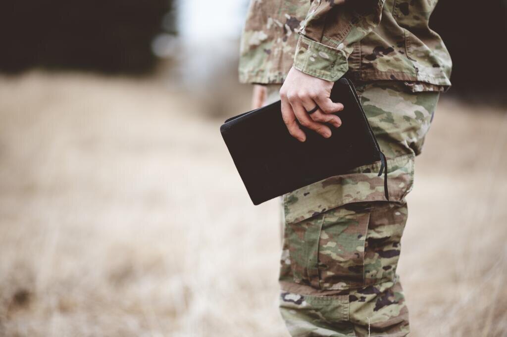    A shallow focus shot of a young soldier holding a bible in a field Журналист