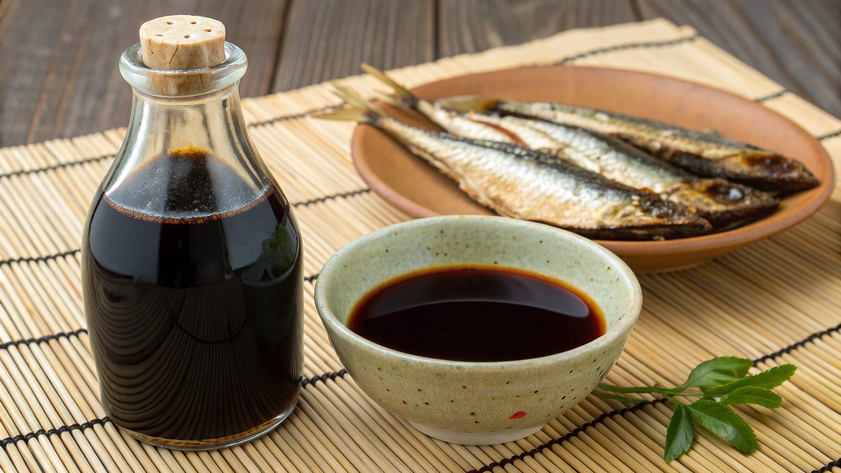 Фото: Стеклянная бутылочка с рыбным соусом. Рядом — пиала с этим соусом и несколько сушеных анчоусов.
