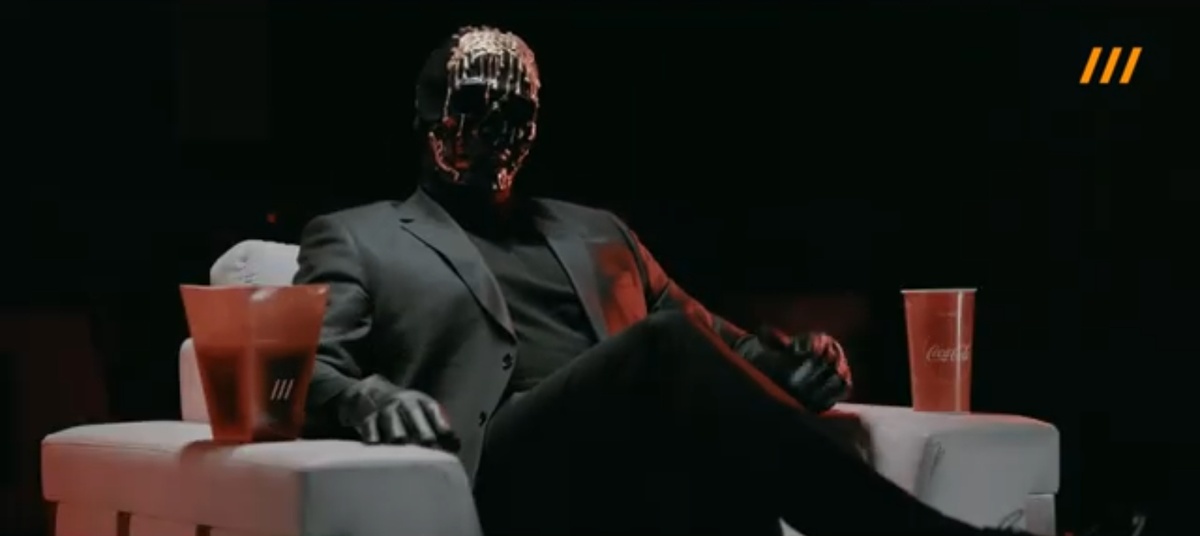 Мориарти в маске и костюме сидит в кресле кинотеатра с попкорном. Это образ эксперта-критика, интеллектуала, а не бандита.