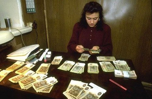 Фото характеризует чуть более ранние времена, когда в ходу были еще советские деньги. Бухгалтер раскладывает зарплату рабтников на столе