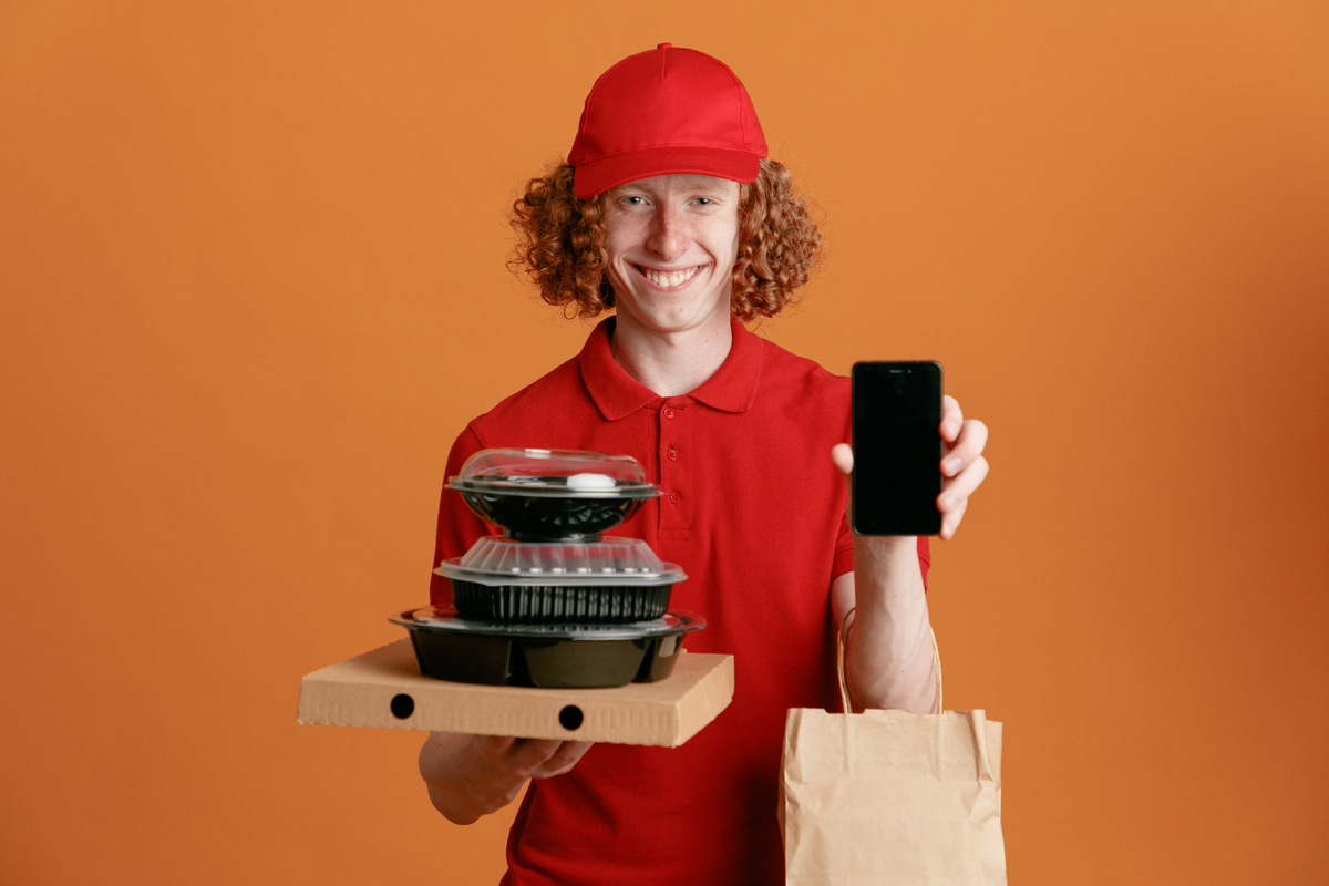 Источник изображения: freepik.com/free-photo/delivery-man-employee-red-cap-blank-tshirt-uniform-holding-pizza-box-food-containers-with-paper-bag-showing-smartphone-happy-positive-smiling-cheerfully-standing-orange-background_27467536.htm