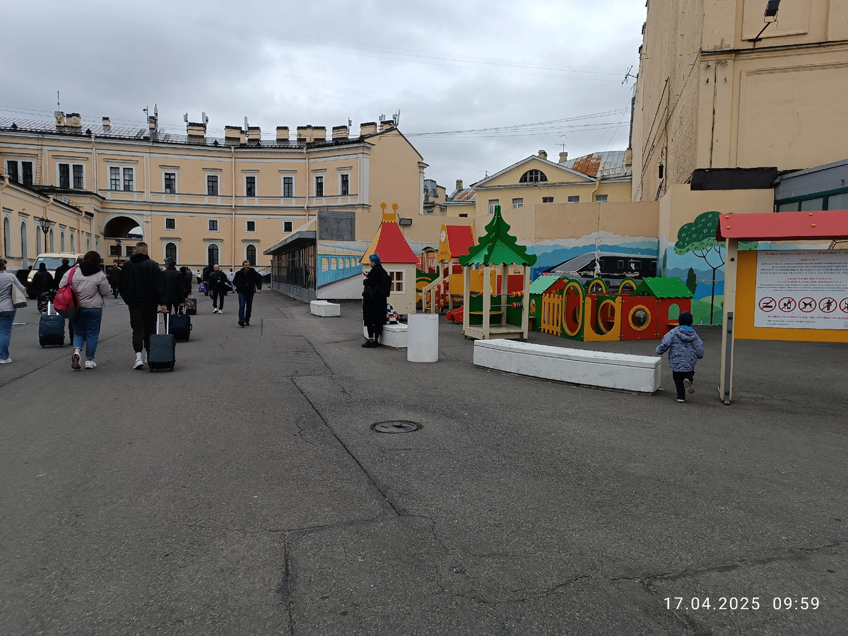 Детская площадка на Московском вокзале в Санкт-Петербурге, и на неё забегает мой Андриан. Невдалеке правее от неё расположен памятник туристам. Через арку выход в город.