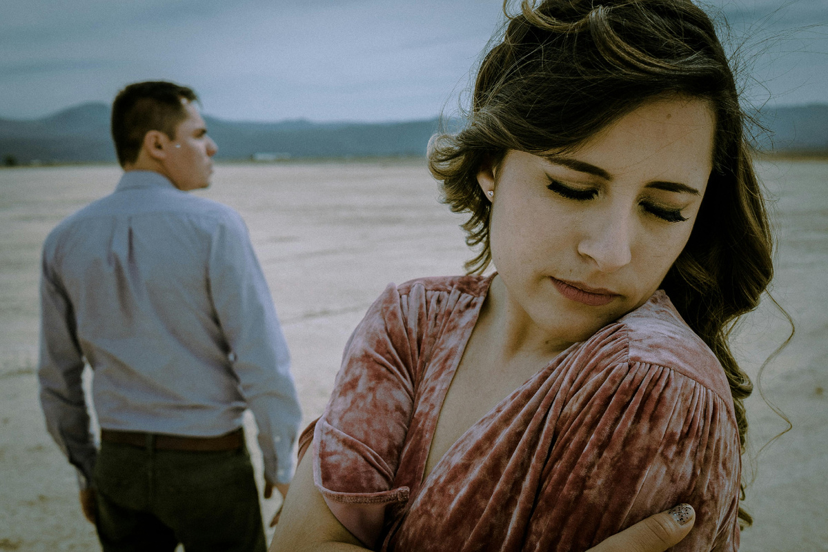 Женщина с грустным выражением лица стоит на переднем плане, а мужчина отходит вдали